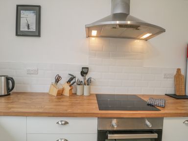A kitchen countertop with a stainless steel kettle knife blocks utensils a cooktop a towel a cutting board and a framed picture on the wall at Sea Change in Newholm near Whitby