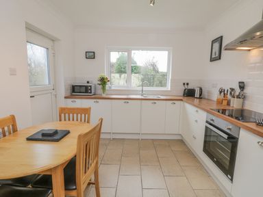 A kitchen with a wooden dining table and chairs a microwave flowers on the counter and a window at Sea Change in Newholm near Whitby