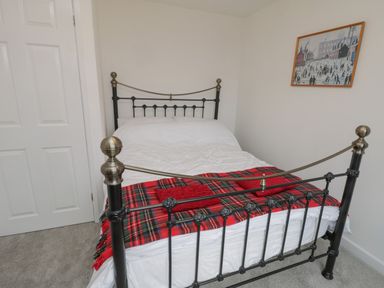 A bedroom with a black metal bed frame a white door a red tartan blanket and a framed picture on the wall at Sea Change in Newholm near Whitby