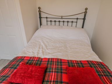 A bedroom with a bed with white bedding and a red plaid blanket with two red pillows at Sea Change in Newholm near Whitby