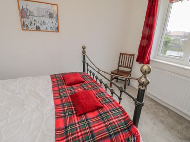 A bedroom with a black metal bed frame a red plaid blanket red cushions a wooden chair a window with red curtains and a painting on the wall at Sea Change Newholm near Whitby