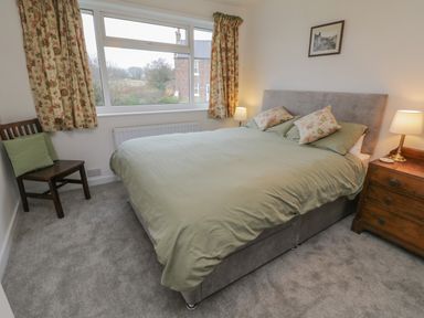 A bedroom with a double bed pillows two lamps a wooden chair and a window with floral curtains at Sea Change in Newholm near Whitby