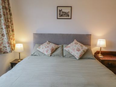 A bedroom with a bed with floral pillows two bedside tables with lamps and a framed picture on the wall at Sea Change in Newholm near Whitby