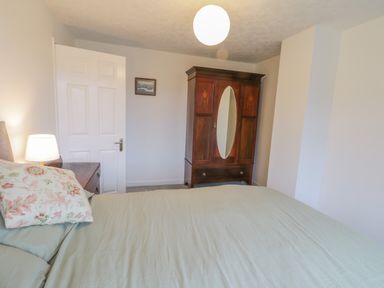 A bedroom with a bed a lamp a wooden wardrobe and a door at Sea Change in Newholm near Whitby