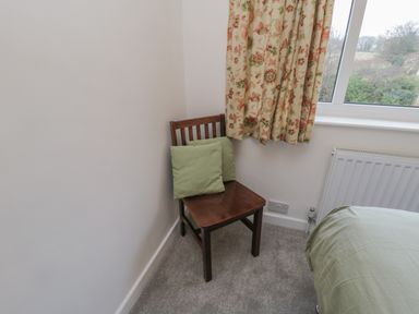 A wooden chair with green cushions beside a window with floral curtains in a bedroom at Sea Change in Newholm near Whitby