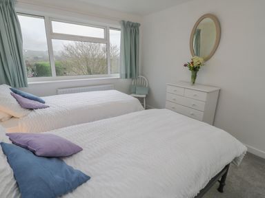 A bedroom with two beds a chest of drawers a mirror and a window with curtains at Sea Change in Newholm near Whitby