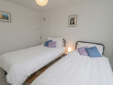 A bedroom with two single beds with white bedding and purple and blue cushions at Sea Change in Newholm near Whitby