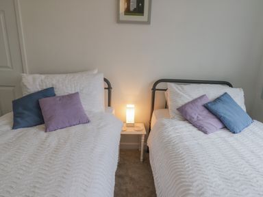 A bedroom with two single beds white bedding and colored pillows with a small table and lamp between them at Sea Change in Newholm near Whitby