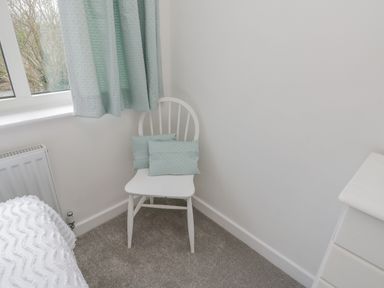 A white wooden chair with two cushions beside a window with curtains in a bedroom at Sea Change in Newholm near Whitby