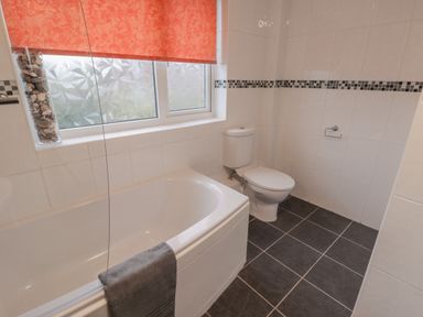 A bathroom with a bathtub a toilet and a window with a red blind at Sea Change in Newholm near Whitby