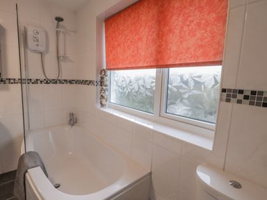 A bathroom with a bathtub shower toilet and a window with a red blind at Sea Change in Newholm near Whitby