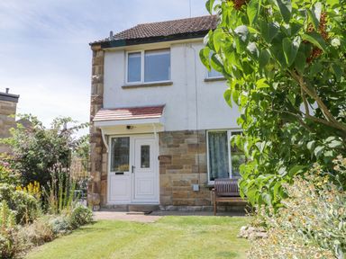 A front view of a two-story house with a garden and bench at Sea Change in Newholm near Whitby