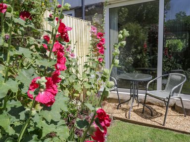 A garden area with red flowers near a patio table and two chairs outside a glass door at Sea Change in Newholm near Whitby