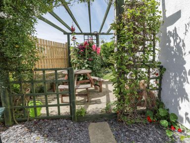 An outdoor patio with wooden picnic table and benches under a pergola with climbing plants at Sea Change in Newholm near Whitby