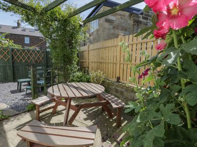 A garden area with a wooden round table and benches next to a wooden fence and plants at Sea Change in Newholm near Whitby