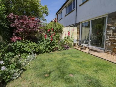 A garden with grass and flowering plants beside a house with sliding glass doors and outdoor chairs at Sea Change in Newholm near Whitby