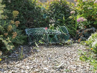 A garden area with flowering plants and lobsters pots on a gravel surface at Sea Change in Newholm near Whitby