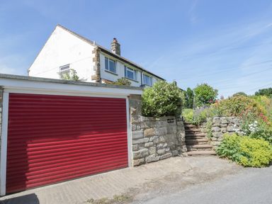 A house with a red garage door and stone steps surrounded by greenery at Sea Change in Newholm near Whitby