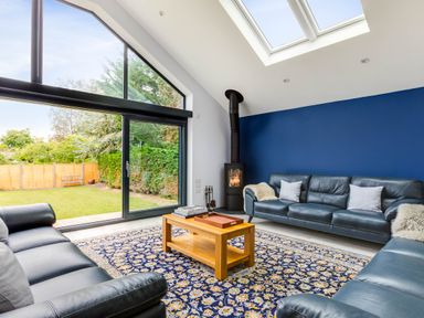 A living room with leather sofas a wooden coffee table a patterned rug a wood-burning stove and large sliding glass doors at The Garden House in Rock