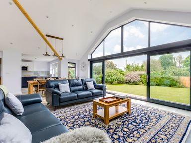 A living room with blue leather sofas and a wooden coffee table on a patterned rug next to large glass sliding doors with garden views at The Garden House in Rock