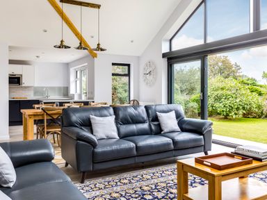 A living room with leather sofas a wooden coffee table rug and large windows showing a garden at The Garden House in Rock