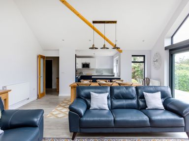 A living room with blue leather sofas and wooden dining table open to a kitchen at The Garden House in Rock