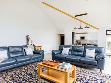 A living room with two blue sofas a wooden coffee table and a patterned rug with a kitchen in the background at The Garden House in Rock
