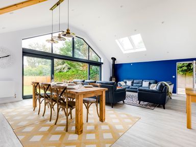 A dining and living area with a wooden table and chairs and blue sofas by a blue wall at The Garden House in Rock