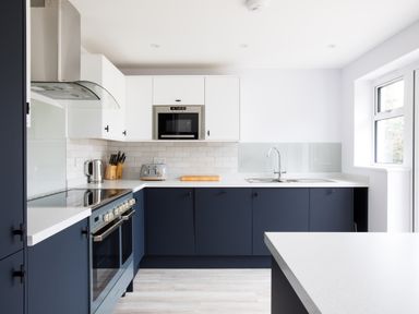 A kitchen with white upper cabinets and black lower cabinets with a stove microwave toaster and sink at The Garden House in Rock