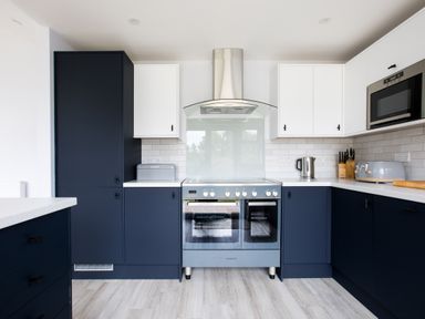 A kitchen with blue and white cabinets a stove a toaster a kettle knives and a microwave at The Garden House in Rock