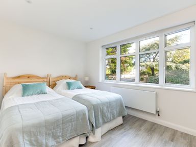 A bedroom with two single beds green pillows a bedside table with lamp and large windows showing trees at The Garden House in Rock