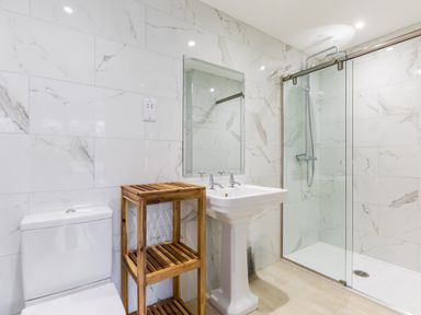 A bathroom with a toilet wooden shelves pedestal sink and a glass shower at The Garden House in Rock