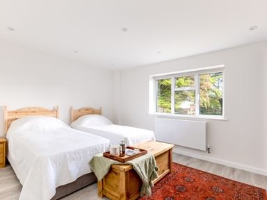 A bedroom with two single beds wooden chest and window showing trees at The Garden House in Rock