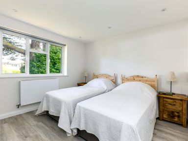A bedroom with two single beds with white bedspreads and wooden headboards a window and two wooden bedside tables with lamps at The Garden House in Rock