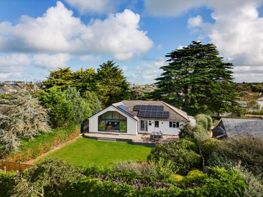 A single story house with solar panels on the roof surrounded by trees and a lawn at The Garden House in Rock