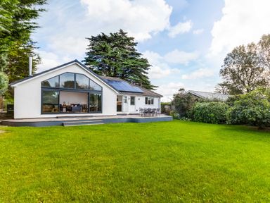 A house with large windows and a patio in a garden with grass and trees at The Garden House in Rock