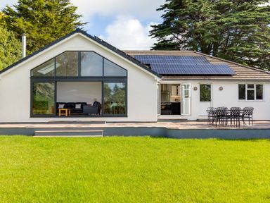 A house with large windows a patio with a table and chairs and solar panels on the roof at The Garden House in Rock