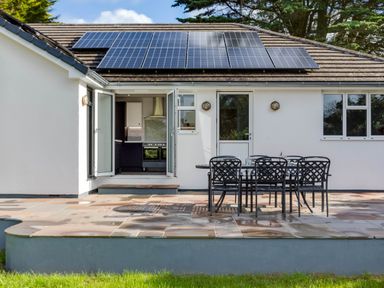 A patio with a metal table and six chairs outside a house with solar panels on the roof at The Garden House in Rock