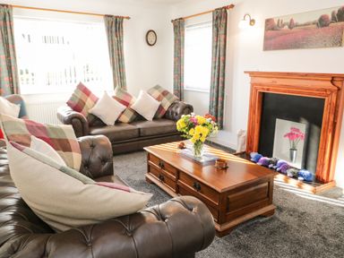 A living room with leather sofas a wooden coffee table with flowers and a fireplace at Gwersyllt in Benllech