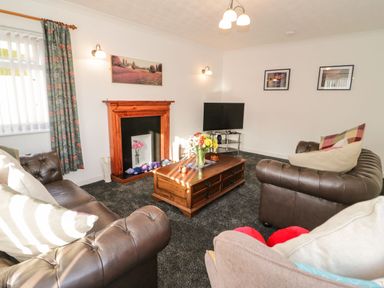 A living room with leather sofas a wooden coffee table a television and a fireplace at Gwersyllt in Benllech