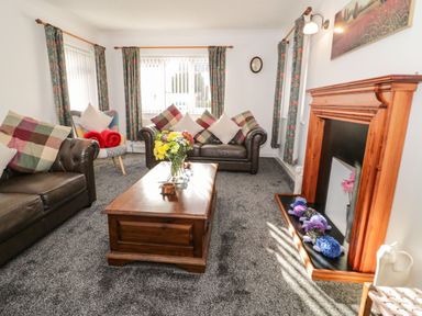 A living room with two leather sofas a wooden coffee table flowers on the table and a fireplace in Gwersyllt Benllech