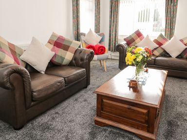 A living room with two leather sofas a wooden coffee table with flowers and a single armchair with cushions and rolled towels at Gwersyllt in Benllech