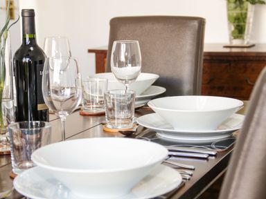 A dining table set with white bowls plates wine glasses water glasses utensils and a wine bottle in Gwersyllt Benllech