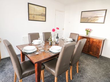 A dining room with a wooden table set for six with leather chairs and two framed pictures on white walls at Gwersyllt in Benllech