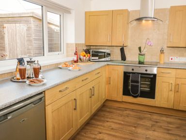A kitchen with wooden cabinets a countertop with food and drinks a window and cooking appliances at Gwersyllt in Benllech