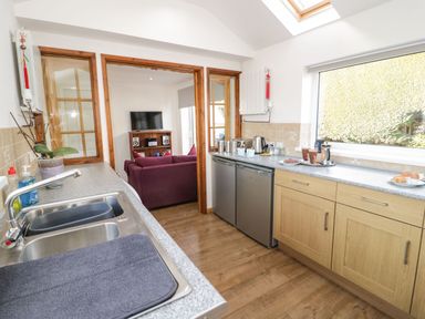 A kitchen with a double sink countertop and appliances next to a living room with a purple sofa and television at Gwersyllt in Benllech