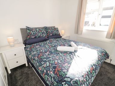 A bedroom with a bed covered in floral bedding two bedside tables with lamps and a window at Gwersyllt in Benllech