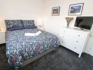 A bedroom with a bed with floral bedding two rolled towels a white dresser TV and pictures on the wall at Gwersyllt in Benllech