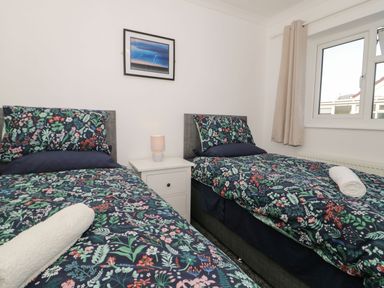 A bedroom with two single beds with floral bedding a white nightstand with a lamp and a window at Gwersyllt in Benllech