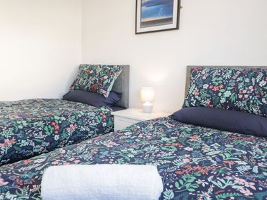 A bedroom with two single beds with floral bedding a white nightstand and lamp in between at Gwersyllt in Benllech